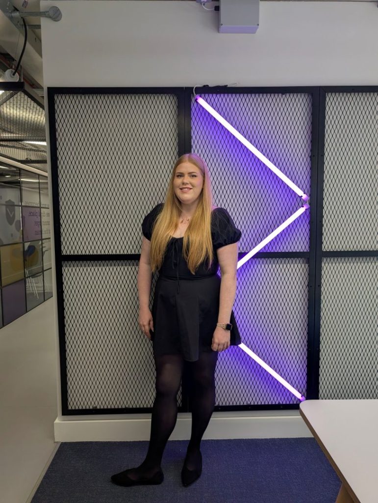 Person standing in front of lit geometric wall with blue and purple lights in an office setting.