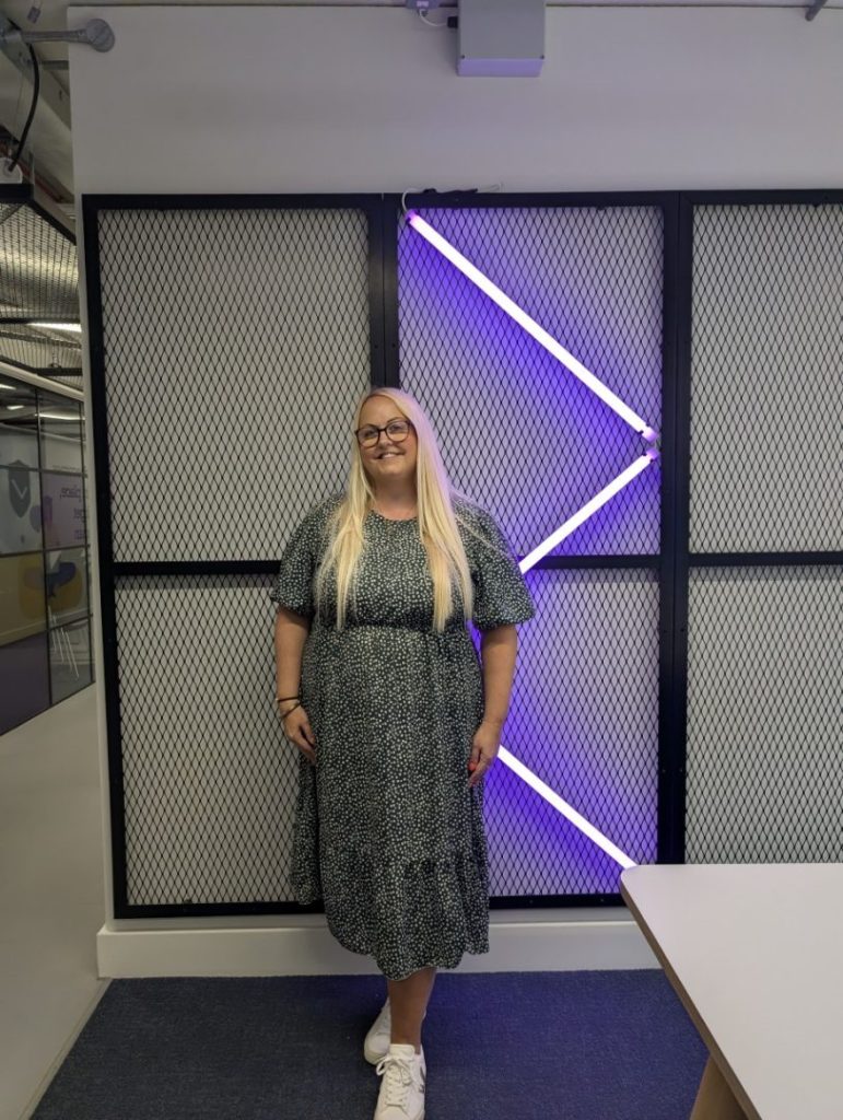 Person standing in front of lit geometric wall with blue and purple lights in an office setting.